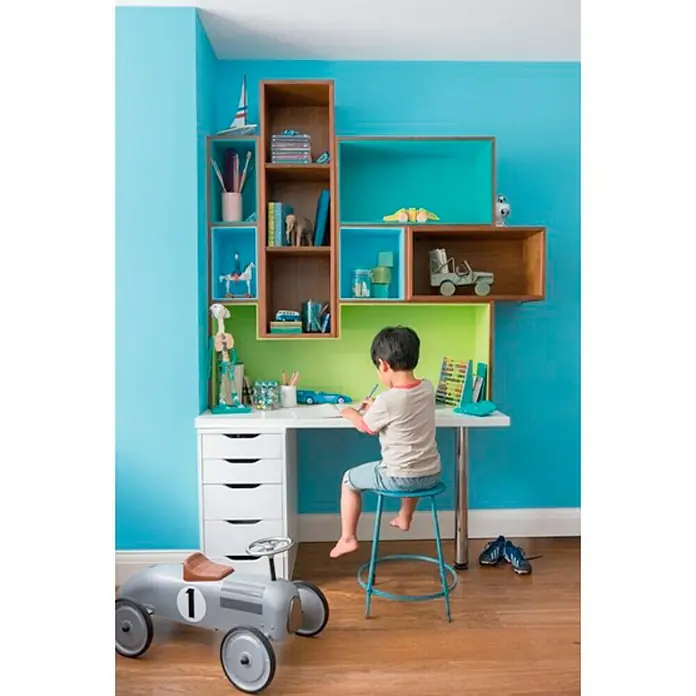 Bruguer Esmalte de color Acrylic Multisuperficie - Azul Caribe, Satinado, 750 ml, Base de agua - Una habitación infantil con un escritorio blanco, estanterías coloridas y un niño dibujando en él.