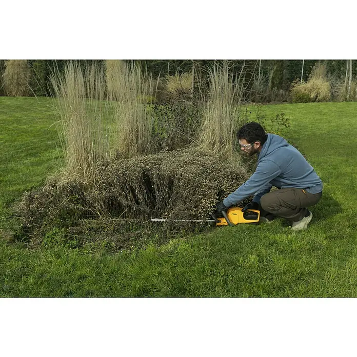 Stiga 100er Serie Akku-Heckenschere HT 100e Set - 20 V, Li-Ionen, 1 Akku, Schnittlänge: 50 cm - Mann, der mit einer Stiga-Heckenschere eine Hecke schneidet. Die gelbe Heckenschere von Stiga ist ein Gartengerät für den perfekten Schnitt.