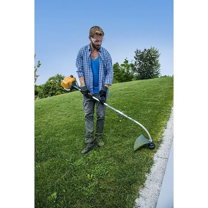 Stiga Benzin-Motorsense GT 330 A - 700 W, Schnittbreite Faden: 38 cm - Ein Mann, der mit einer Motorsense einen Rasen trimmt. Das gelbe Gerät ist im Betrieb und schneidet das Gras präzise.