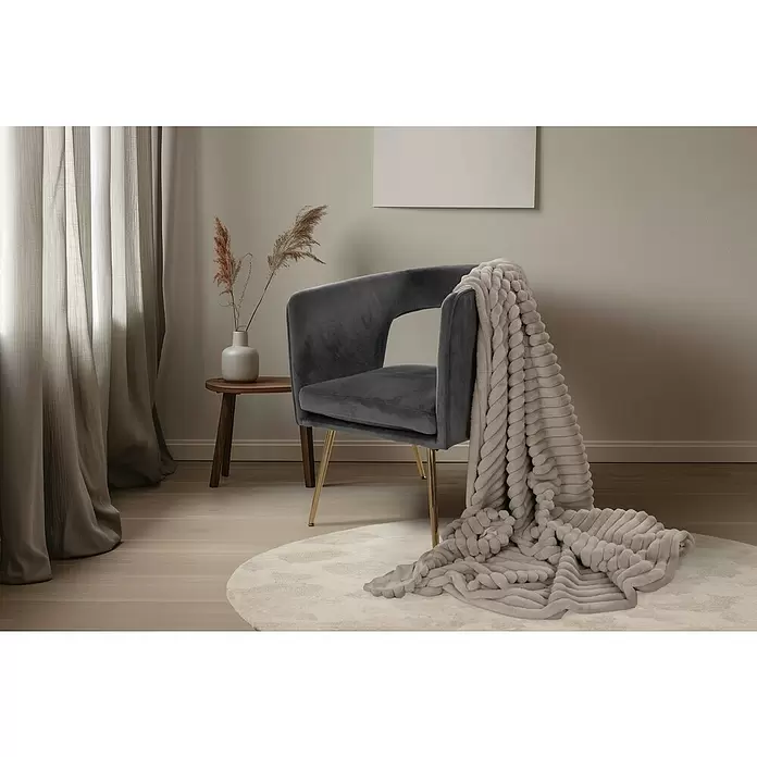 Manta para sofá Plush - 150 x 200 cm, Topo - Sillón de terciopelo gris oscuro con patas doradas y una manta suave gris claro texturizada, en una sala acogedora.