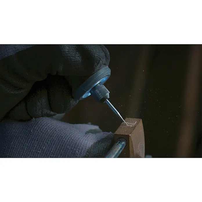 Dremel Graviermesser 105 - Arbeitsdurchmesser: 0,8 mm, 3 Stk. - Nahaufnahme eines Werkzeugs, das präzise ein Objekt bearbeitet, wobei Schutzhandschuhe und feine Staubpartikel die Szene ergänzen.