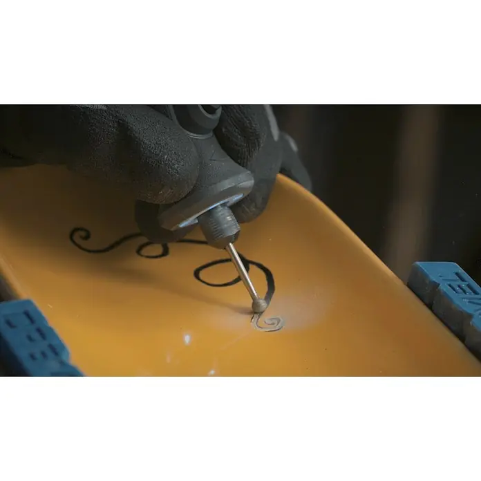 Dremel Diamant-Schleifstifte Mod. 7105 - Durchmesser Kopf: 4,4 mm, 2 Stk. - Nahaufnahme eines gelben Objekts, das mit einem Dremel und einem Kugelfräser mit einem Wirbelmuster graviert wird, wobei der Bediener Handschuhe trägt.