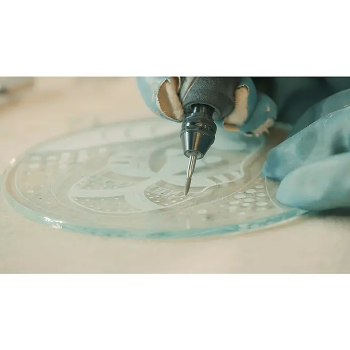Dremel Diamant-Schleifstifte Mod. 7144 - Durchmesser Kopf: 2,4 mm, 2 Stk. - Nahaufnahme von einem Glasgravurwerkzeug, das ein filigranes Muster in eine runde Glasplatte graviert, präzise und detailliert.