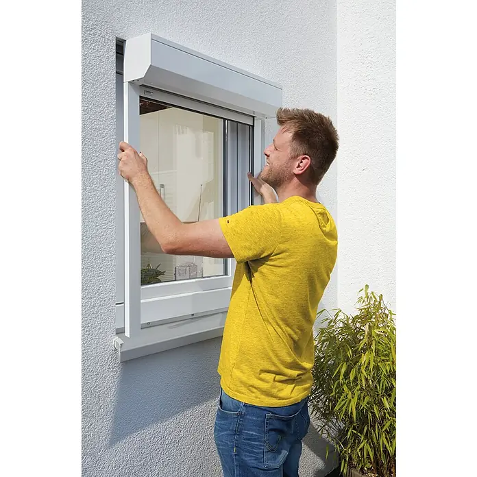 Schellenberg Rollladen-Komplett-Set MINIVorbau, 95 x 140 cm - Ein Mann montiert ein Rollladensystem an einem Fenster, um die Energieeffizienz und Sicherheit des Hauses zu verbessern.