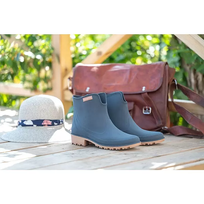 Black Fox Stiefelette Preston - Schuhgröße: 42, Blau - Dunkelgraue Gummistiefel mit braunen Sohlen, auf Holz präsentiert mit Strohhut und Ledertasche.