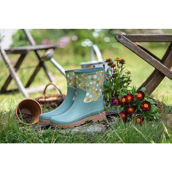 Black Fox Gummistiefel Lizia - Schuhgröße: 38, Grün - Ein Paar Blackfox-Gartenstiefel mit Blumenmuster stehen im Gras, umgeben von Gartengeräten.