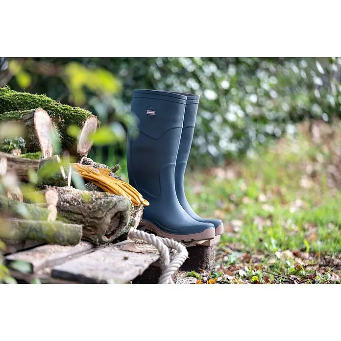 Black Fox Gummistiefel Fox - Schuhgröße: 42, Grün - Abgebildet sind Blackfox-Gummistiefel, kombiniert mit Holz, Moos, alten Brettern und gelben Handschuhen, wodurch ein rustikaler Look entsteht.