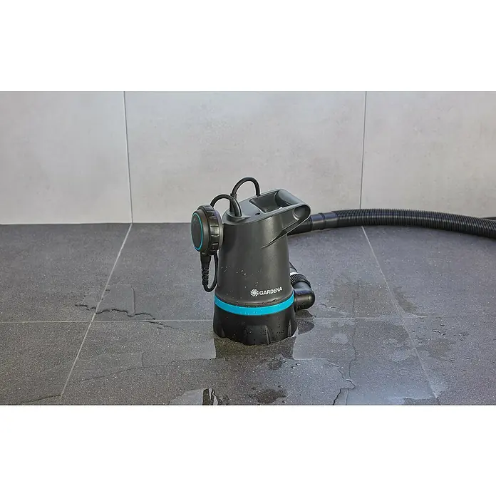 Gardena Klarwasser-Tauchpumpe 20000 Basic - 550 W, Max. Fördermenge: 20.000 l/h - Eine Gardena Schmutzwasser-Tauchpumpe mit blauem Akzent steht auf einem gefliesten Boden mit Wasserspritzern, ein Schlauch liegt daneben.