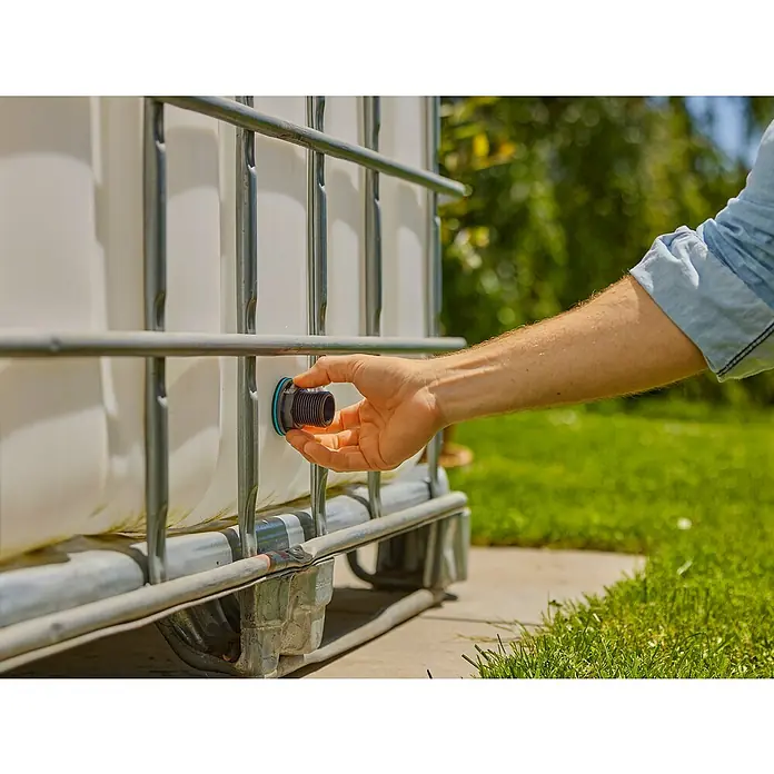 Gardena Anschlussstück Push In G1"-G3/4"Passend für: Wassertanks mit 2-10 mm Wandstärke & Radius von min. 50 cm - Ein Mann befestigt einen schwarzen Wasserhahn an einem IBC-Wassertank im Freien. Praktische Bewässerungslösung für den Garten.