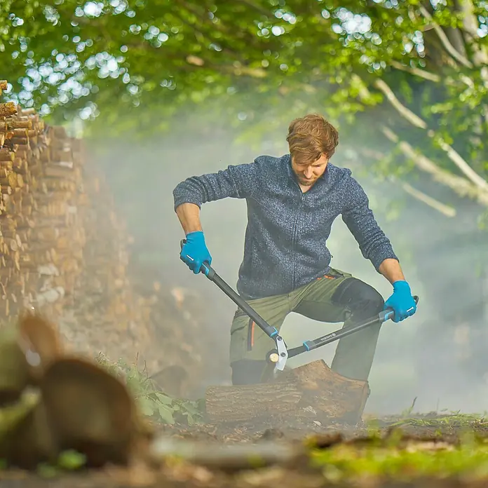 Gardena EnergyCut Astschere Pro L - Schneidsystem Gartenschere: Bypass, Max. Aststärke: 50 mm - Ein Mann kniet und schneidet ein Stück Holz mit einer Gardena Astschere. Die Astschere ist ideal für das Zuschneiden dicker Äste.