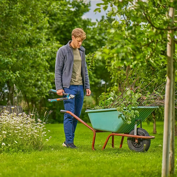 Gardena Astschere TeleCut Pro S - Max. Aststärke: 50 mm - Ein Mann steht mit einer Astschere neben einer Schubkarre voller Äste, bereit für die Gartenarbeit.