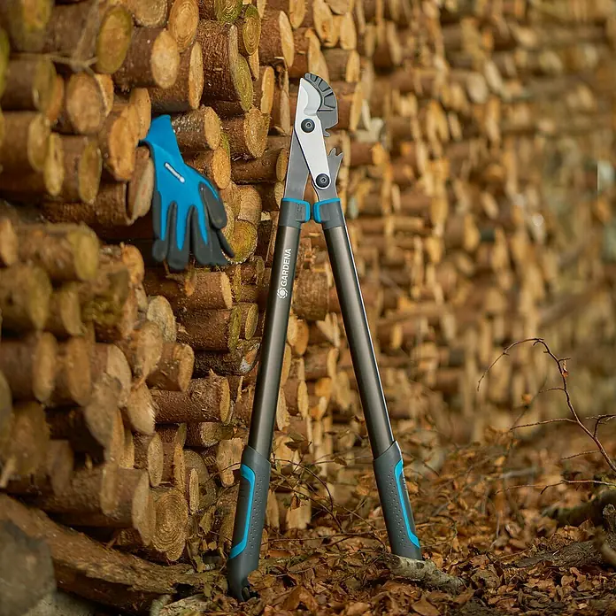 Gardena EnergyCut Astschere Pro L - Schneidsystem Gartenschere: Amboss, Max. Aststärke: 50 mm - Gardena Astschere mit blauen Gartenhandschuhen vor einem Holzstapel. Die Astschere ist gut sichtbar und steht im Vordergrund.
