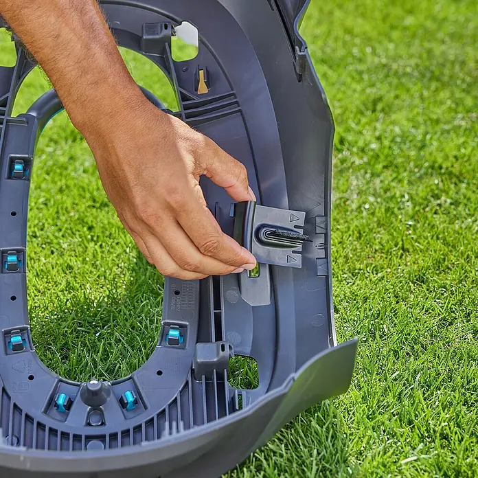Gardena Bürsten-Set für Rasenmäher - Gardena Mähroboter smart SILENO pro, smart SILENO max und smart SILENO free - Eine Person befestigt ein schwarzes Teil an einem Rasenmäher-Roboter. Das Teil wird in die entsprechende Öffnung eingesetzt. Der Hintergrund ist grünes Gras.