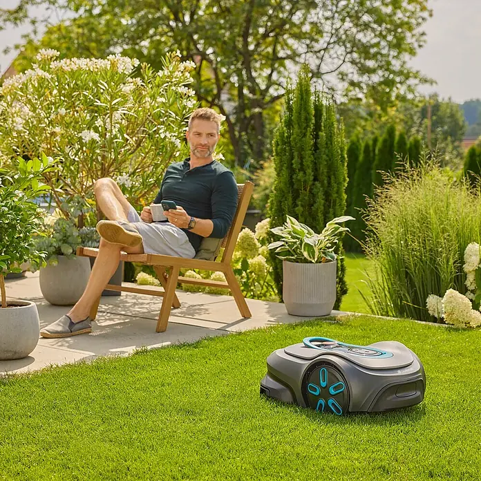 Gardena Mähroboter smart SILENO pro 600 m² - 600 m², Schnittbreite: 16 cm, Induktionsgestützte Navigation, Begrenzungskabel - Bild von einem GARDENA Mähroboter mit einem Mann, der sich entspannt zurücklehnt, während der Rasen gemäht wird.