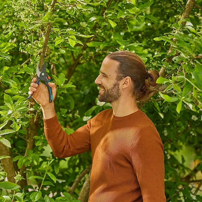 Gardena Gartenschere PremiumCut Pro - Bypass, Max. Aststärke: 24 mm - Ein Mann mit einer Gartenschere schneidet Äste in einem üppigen Garten. Die Schere ist scharf und präzise für den perfekten Schnitt.