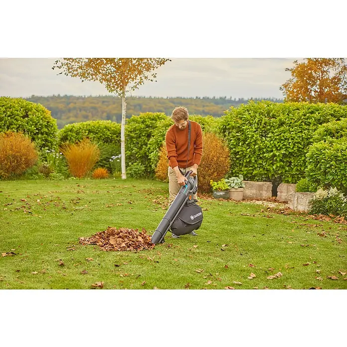 Gardena Power for All 18V Akku-Laubsauger & -Laubbläser PowerJetCollect - 18 V, 1 Akku, 4 Ah, Blasgeschwindigkeit: 250 km/h - Ein Mann benutzt einen Gardena-Laubsauger, um Blätter in einem gepflegten Garten zusammenzusaugen. Das Gerät ist ideal für die Gartenarbeit.