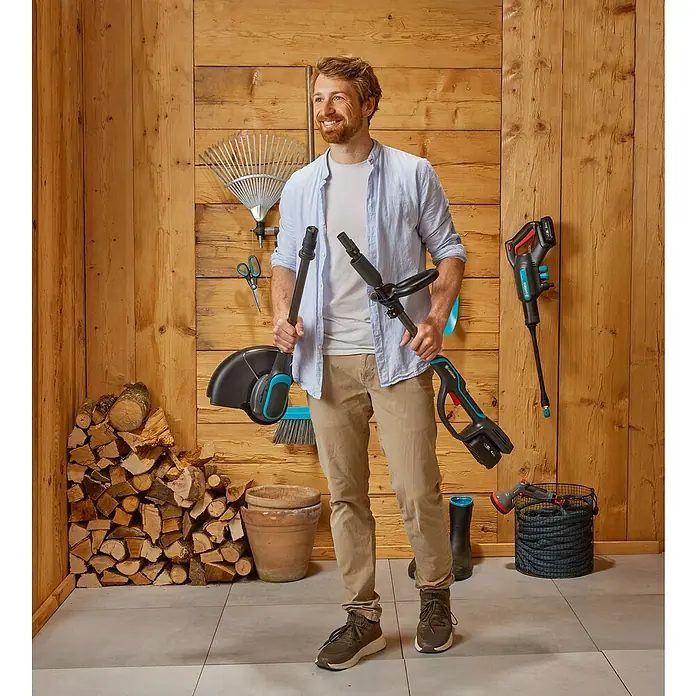 Gardena Power for All 18V Akku-Rasentrimmer PowerTrim 30/18V - 18 V, Li-Ionen, Ohne Akku, Schnittbreite Faden: 30 cm - Ein Mann steht in einem Raum mit Gartengeräten, darunter eine Heckenschere, ein Rasentrimmer und eine Gartenspritze.