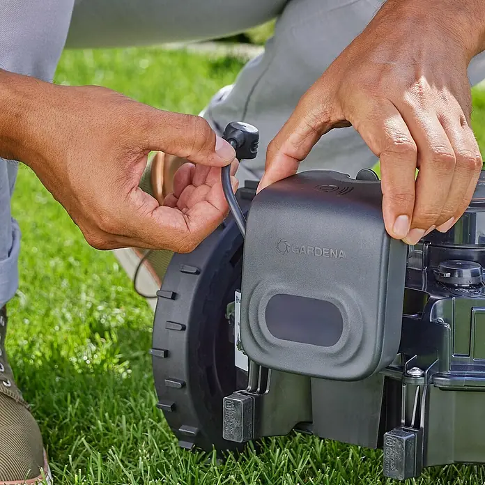 Gardena Antikollisionsradar für Mähroboter - Gardena Mähroboter smart SILENO pro, smart SILENO max, smart SILENO free - Nahaufnahme eines Mannes, der ein Kabel an einen Gardena-Rasenmäher anschließt.