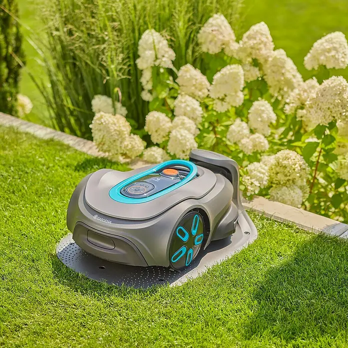 Gardena Mähroboter smart SILENO max - 1.500 m², Schnittbreite: 22 cm, Induktionsgestützte Navigation, Begrenzungskabel - Der Gardena Mähroboter ist auf seiner Ladestation, umgeben von saftigem, grünem Gras und blühenden Pflanzen.