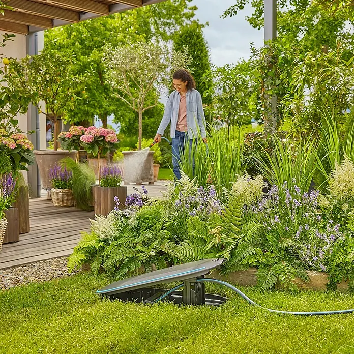 Gardena Schlauchbox Undercover RollUp - Schlauchlänge: 20 m - Eine Frau gießt den Garten mit einem Gardena Flächenregner AquaZoom. Präzise und gleichmäßige Bewässerung für gesunde Pflanzen.