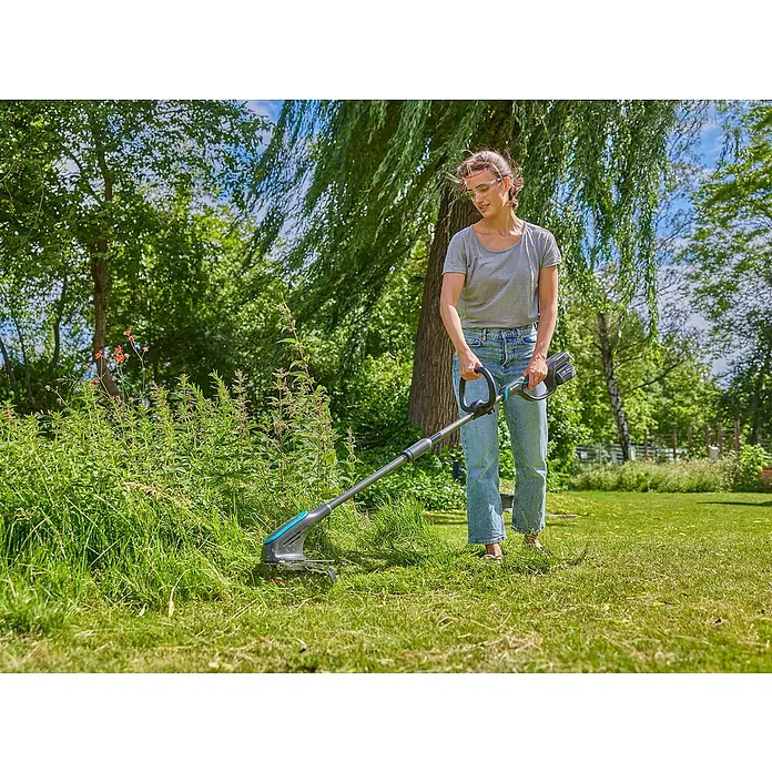 Gardena Power for All 18V Akku-Rasentrimmer PowerTrim 30/18V - 18 V, Li-Ionen, Ohne Akku, Schnittbreite Faden: 30 cm - Frau schneidet Gras mit Akku-Rasentrimmer. Der Trimmer ist blau/grau und hat einen Akku.