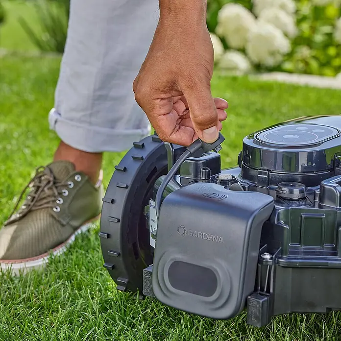 Gardena Antikollisionsradar für Mähroboter - Gardena Mähroboter smart SILENO pro, smart SILENO max, smart SILENO free - Detailaufnahme eines Gardena Rasenmähroboters mit einer Person, die ein Kabel anschließt. Der Fokus liegt auf der Funktionalität des Produkts.