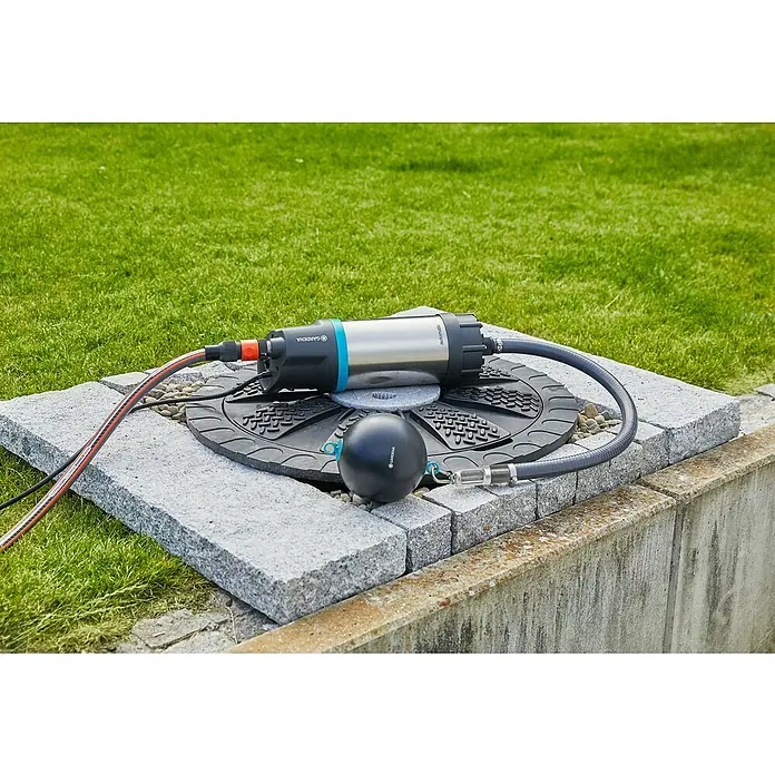 Gardena Rückflussverhinderer - Passend für: Saugschlauch-Durchmesser: 19 mm (3/4") / 25 mm (1") - Eine Gardena Regenfasspumpe mit Kabel und Schlauch liegt auf einem grauen Stein, eingebettet in Rasen.