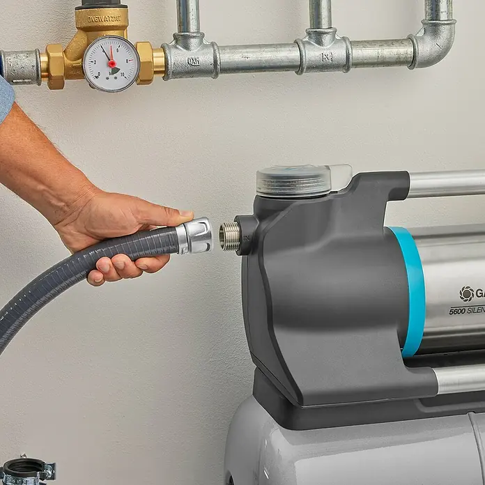 Gardena Sauggarnitur 25 mm 1" 4 m - Durchmesser: 25 mm, Länge: 4 m - Eine Gardena Hauswasserautomat-Pumpe wird an einen grauen Wasserschlauch angeschlossen. Das Produkt ist hochwertig und effizient.