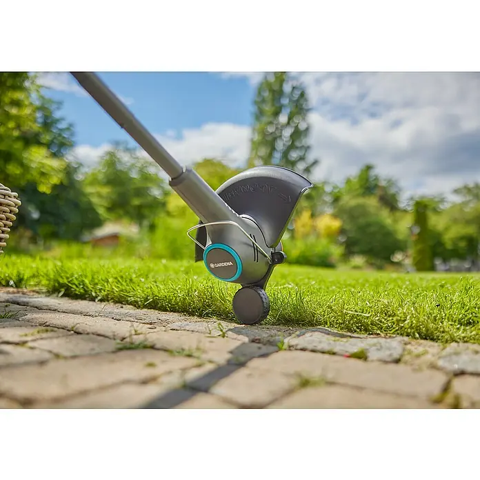 Gardena Power for All 18V Akku-Rasentrimmer EasyTrim 25/18V - 18 V, 2 Ah, Li-Ionen, 1 Akku, Schnittbreite Faden: 25 cm - Detailaufnahme eines Gardena Trimmers, der Rasen an einer Steinmauer trimmt, mit Fokus auf Präzision und einfacher Handhabung.
