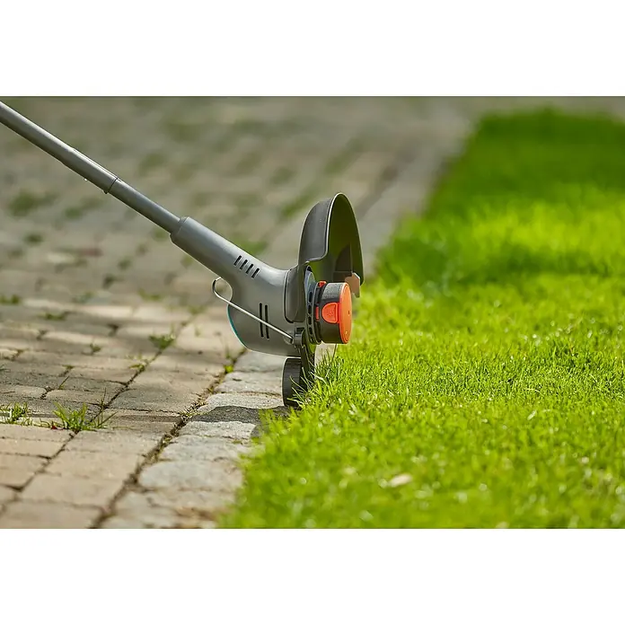 Gardena Ersatzfadenspule - Fadenlänge: 4 m, Fadenstärke: 1,6 mm, Passend für: EasyTrim-Modelle von GARDENA - Nahaufnahme eines Rasentrimmers, der an einer gepflasterten Fläche entlang einer Rasenkante arbeitet und das Gras sauber abschneidet.