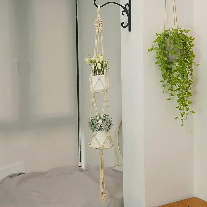 Blumenampel Makramee - Ø x H: 4 x 120 cm, Beige - Ein mehrstöckiger Makramee-Pflanzenhänger mit zwei weißen Töpfen, die jeweils eine Pflanze enthalten, hängt an einer dekorativen Halterung.