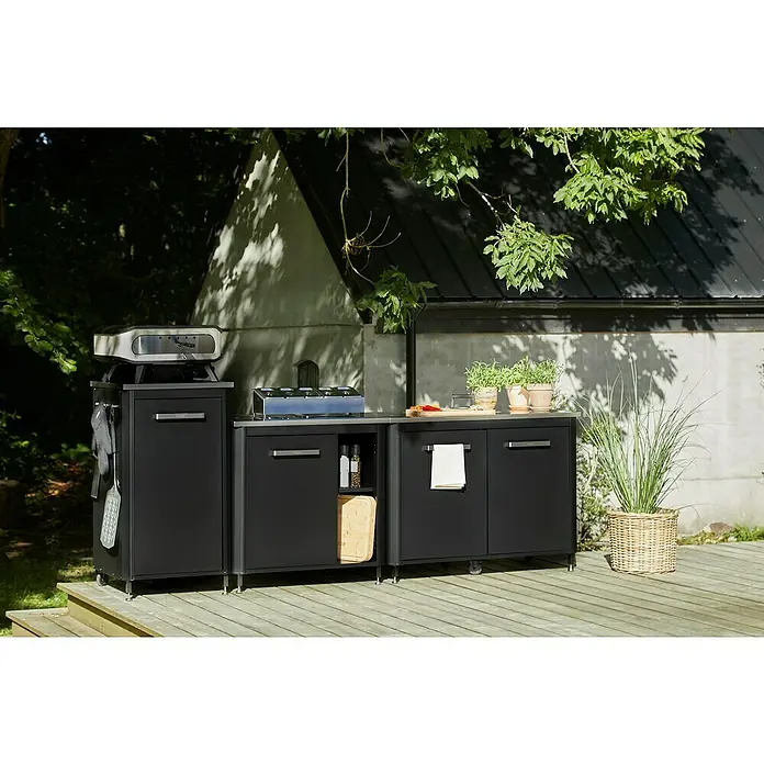 Cozze Outdoorküchen-Modul - Schwarz, B x T x H: 93,5 x 67 x 90 cm - Schwarze Outdoorküche mit Grill, Kochfeld und Schränken auf einer Holzterrasse. Pflanzen und Kochutensilien sind auch auf der Arbeitsfläche vorhanden.