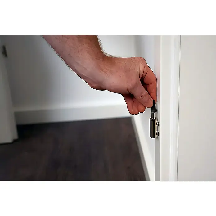 Türbandhaube TÜHZDE - Schwarz, Aufbauhöhe 2 mm - Ein Arm drückt einen Türstopper mit Gummispitze an einer weißen Tür, um das Zuschlagen der Tür zu verhindern.