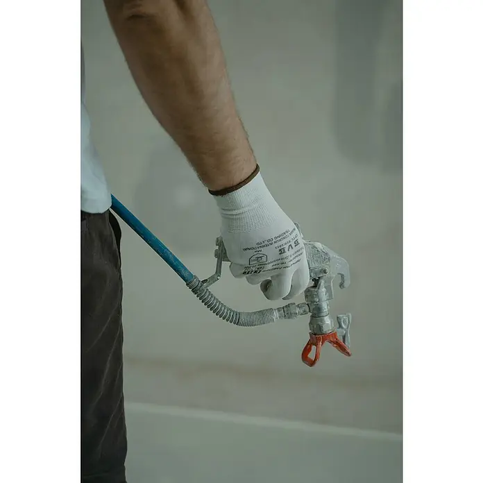 Graco Magnum Sistema de pulverización de pintura A100 Proplus - Caudal: 1,8 l/min, Velocidad de trabajo: 18 m²/min - Primer plano de una mano con guante sosteniendo un pulverizador de pintura con manguera azul, ideal para proyectos de pintura.