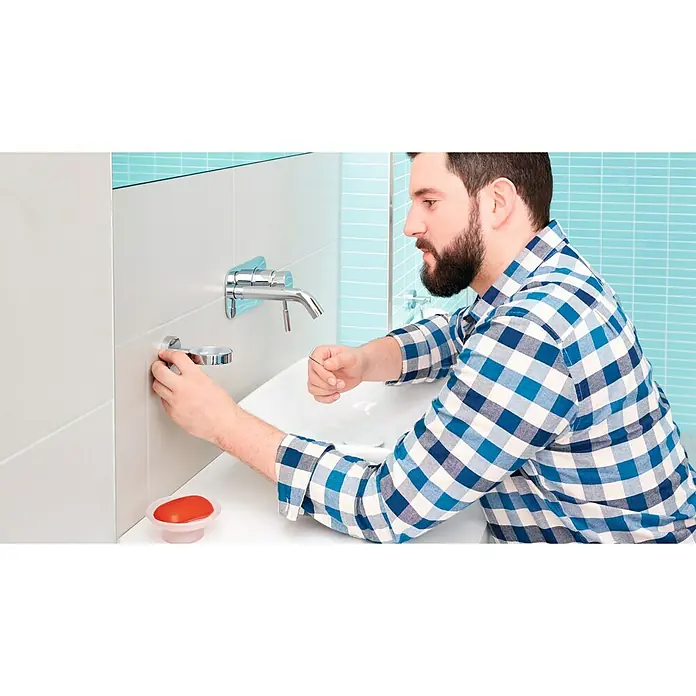 Tesa Smooz Seifenschale - Mit Halterung, Satiniert/Chrom, Glänzend - Ein Mann befestigt eine elegante Seifenablage unter einem modernen Wasserhahn im Badezimmer.