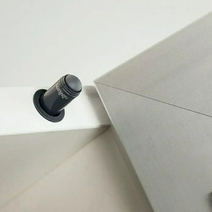 Häfele Amortiguador de puerta para muebles - profundidad de entrada: 50 mm, Plástico - Primer plano de un dispositivo Blum Tip-On gris montado sobre una superficie blanca, diseñado para abrir suavemente las puertas del armario con un toque.