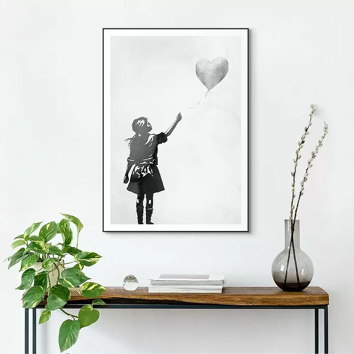 Reinders Bild Slim Frame Black - Balloon Girl, B x H: 50 x 70 cm - Gerahmter Graustufen-Druck eines Mädchens, das nach einem Herzballon greift, hängt über einem Holztisch an der Wand.