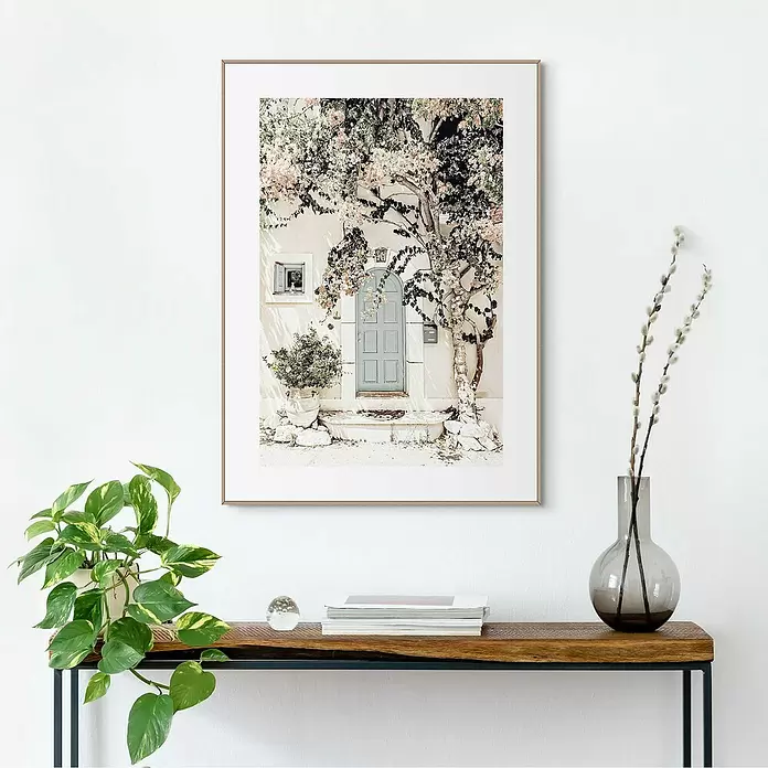 Reinders Bild Slim Frame Wood - Mediteran Door, B x H: 50 x 70 cm - Gerahmter Kunstdruck einer hellblauen Tür, umgeben von rosa blühenden Bäumen, hängend über einem Holzkonsolentisch.