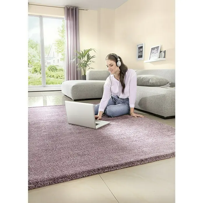 Kurzflorteppich Softtouch - Pastell-Lila, 150 x 80 cm, 100 % Polypropylen (Flor) - Nahaufnahme eines flauschigen, violetten Teppichs, auf dem eine Frau mit Laptop sitzt, ideal für Komfort und Stil in Ihrem Zuhause.