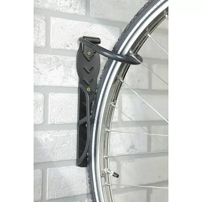 Mottez Gancho de pared para bicicletas B865V - Acero, Negro - Soporte de pared negro de metal para bicicleta, sujetando una rueda contra una pared de ladrillo claro.