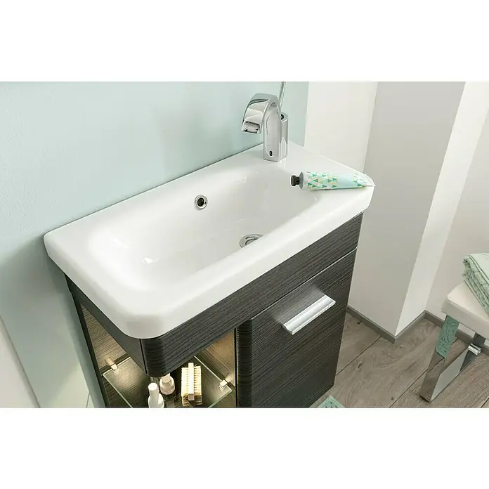 Camargue Faro Mini Einbauwaschbecken - 60 x 30 cm, Weiß - Modernes Badezimmer-Waschbecken mit grauem Unterschrank, minimalistischem Design und Armatur. Eine Tube Handcreme liegt auf dem Beckenrand.