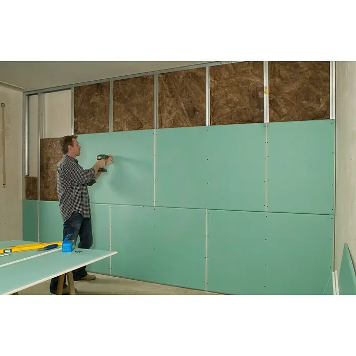 Knauf Gipskartonplatte Top 2000 GKFI - 1.250 x 900 x 12,5 mm, Imprägniert - Ein Mann befestigt grüne Gipskartonplatten an einer Wand mit einer Bohrmaschine. Die Wand hat eine Isolierung und Metallrahmen.