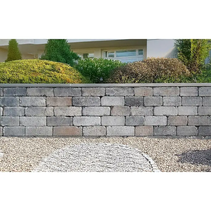 Mauerstein Times Antik Light - 30 x 14 x 12 cm, Muschelkalk, Beton - Graue Mauer aus Betonsteinen mit Pflanzen auf der Oberseite und Kies davor, die eine attraktive und funktionale Gartengestaltung bietet.
