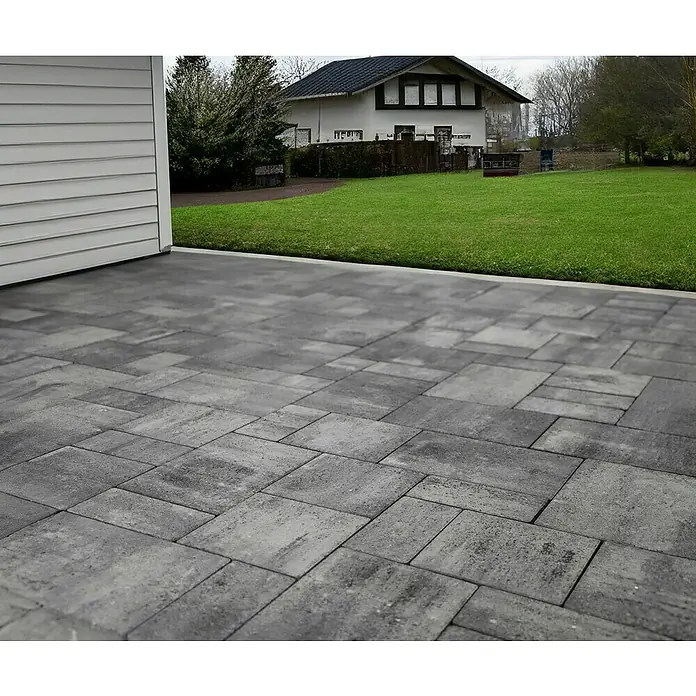 EHL Pflasterstein Fortaleza - Weiß/Anthrazit, Gesamtstückzahl: 27 Stk., Rechteckig - Pflastersteine aus grauem Beton bilden eine Terrasse neben einem Rasen. Das Pflaster hat ein interessantes, unregelmäßiges Muster.
