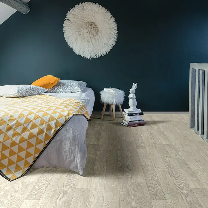 Beauflor PVC-Boden Meterware Sherwood - 400 cm, White Oak 167S, Beige - Ein helles Laminat- oder Vinylbodenmuster in einem Schlafzimmer mit gelber Tagesdecke, das die natürliche Holzmaserung und die Textur hervorhebt.