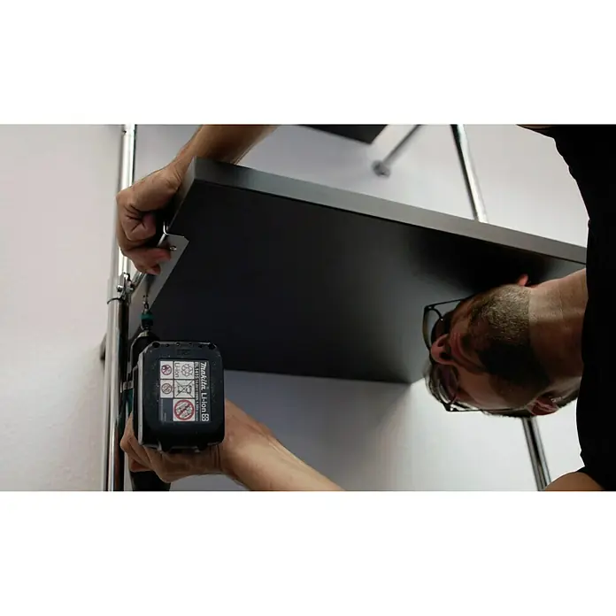 Easy Connect Regalbodenträger - Passend für: Easy Connect Regalsystem, 2 Stk. - Nahaufnahme eines Mannes, der mit einem Akkuschrauber eine schwarze Tischplatte montiert. Im Fokus steht der Akkuschrauber.