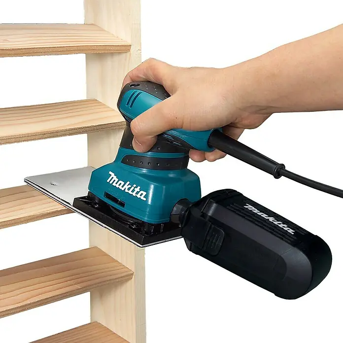 Makita Lijadora orbital eléctrica BO4566 - 200 W - Lijadora orbital Makita en acción, lijando estantes de madera, operada a mano para resultados precisos.