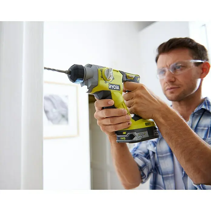 Ryobi ONE+ Akku-Kombihammer R18SDS-125S - 18 V, 1 Akku, 2,5 Ah, 1,3 J - Nahaufnahme eines Mannes, der mit einer gelben Ryobi Bohrmaschine arbeitet. Der Fokus liegt auf der Bohrmaschine und dem Bohrvorgang in der Wand.