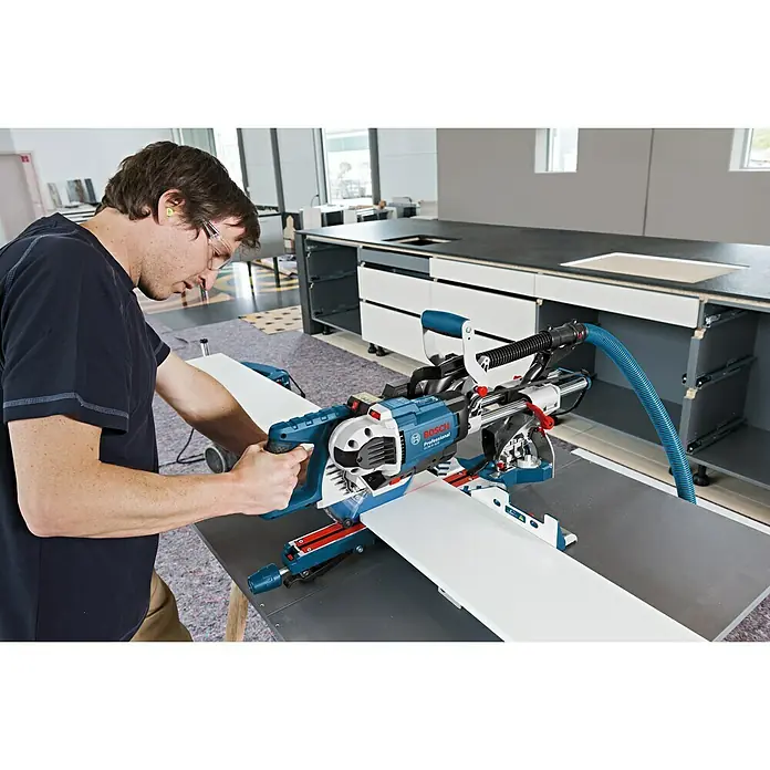 Bosch Professional Paneelsäge GCM 8 SDE - 1.600 W, Durchmesser Sägeblatt: 216 mm - Ein Mann bedient eine Bosch Professional Kapp- und Gehrungssäge. Das Werkzeug ist auf einem Tisch montiert und schneidet ein weißes Brett.