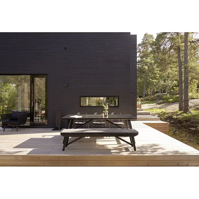 SENSUM Gartenbank - B x T x H: 192 x 38 x 43 cm, Eukalyptus, Schwarz - Ein dunkler Gartentisch mit Stühlen und Bank steht auf einer hölzernen Terrasse neben einem modernen Haus.